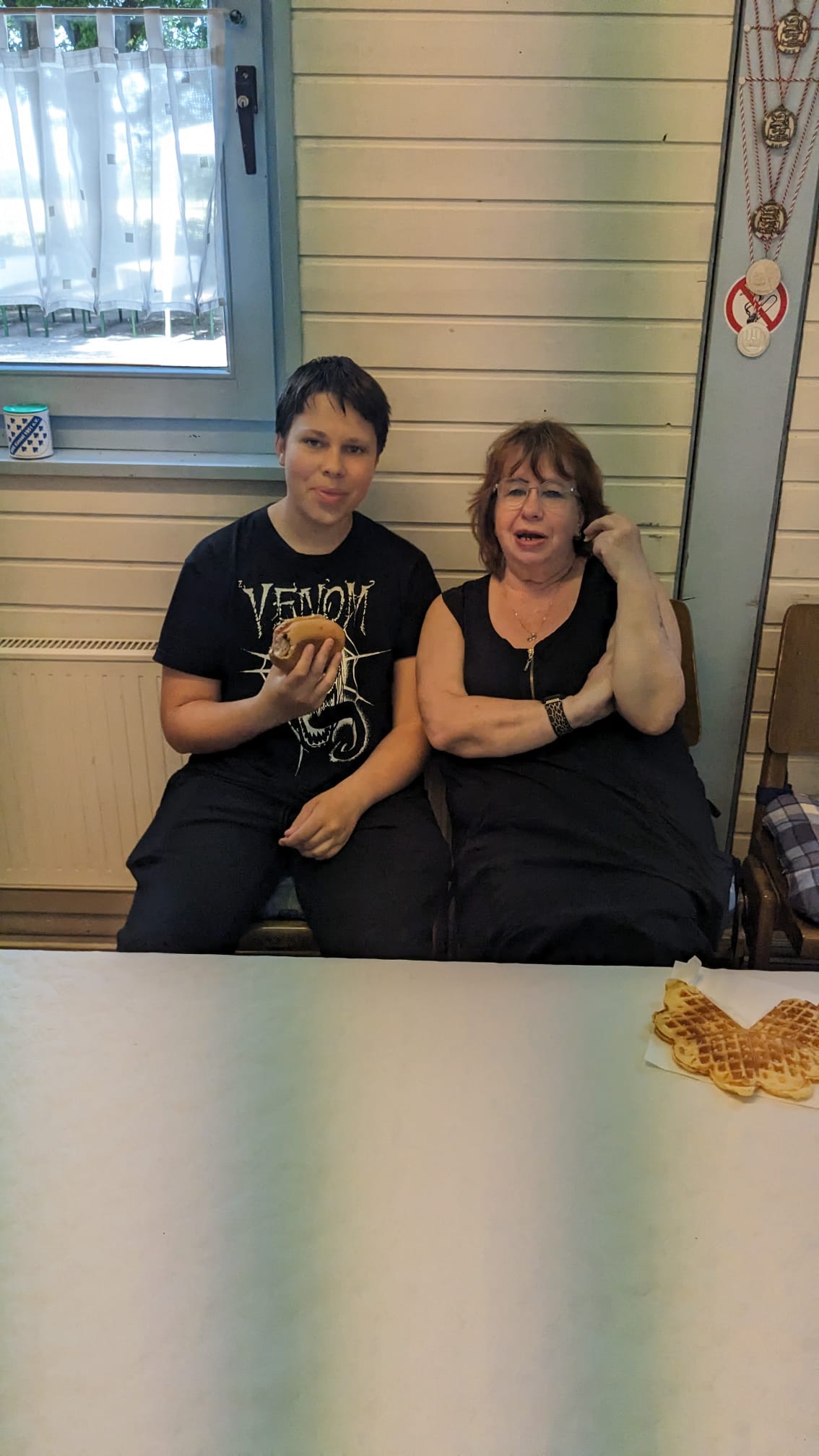 Ein Junge und eine Frau sitzen an einem Tisch, der Junge hält ein Brötchen, daneben liegt eine Waffel