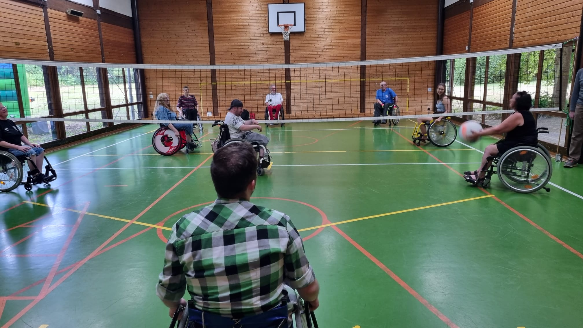 Menschen in Rollstühlen spielen gemeinsam Sitzvolleyball in einer Turnhalle.