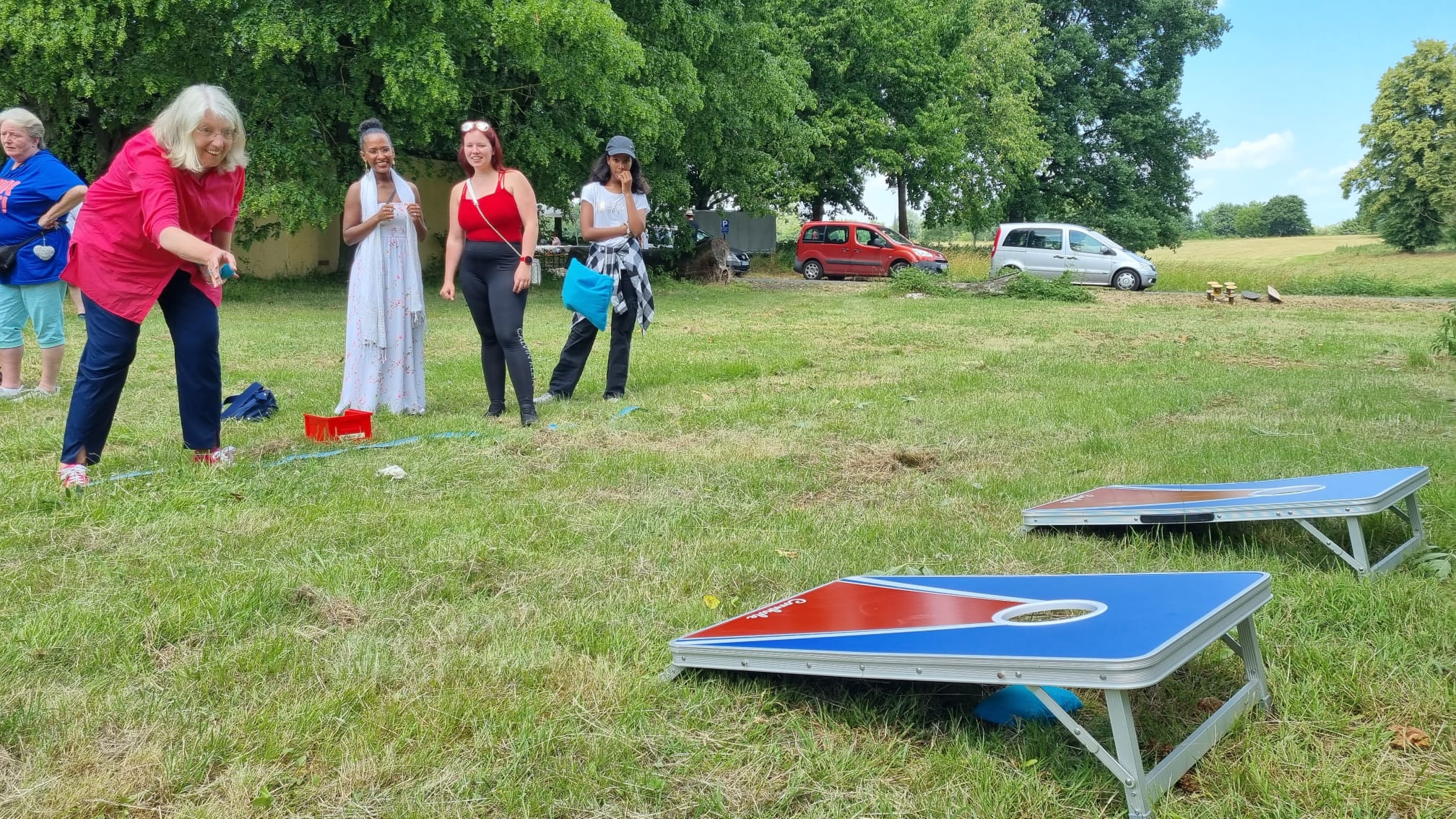 Eine Frau wirft ein Beanbag auf ein Cornhole-Spiel, während vier andere Frauen zusehen und lächeln