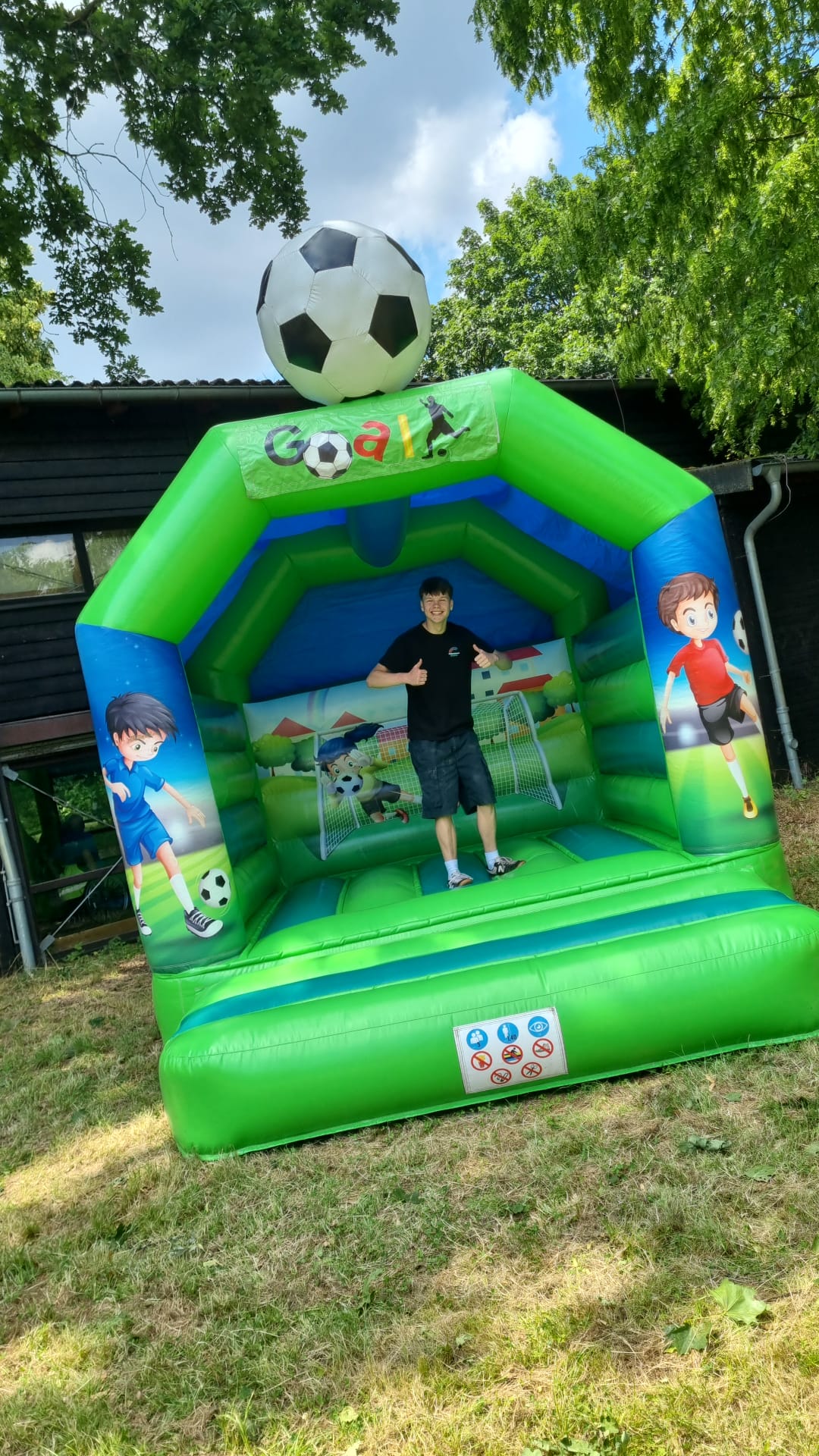 Eine grüne Hüpfburg mit Fußballmotiv, darauf steht eine Person mit Daumen nach oben